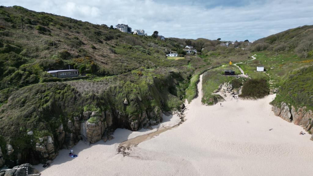 Lot: 69 - DETACHED RESIDENTIAL PROPERTY ENJOYING BREATHTAKING SEA VIEWS IN TRULY STUNNING LOCATION - Drone photo taken from over the sea looking up the beach towards Porthcurno